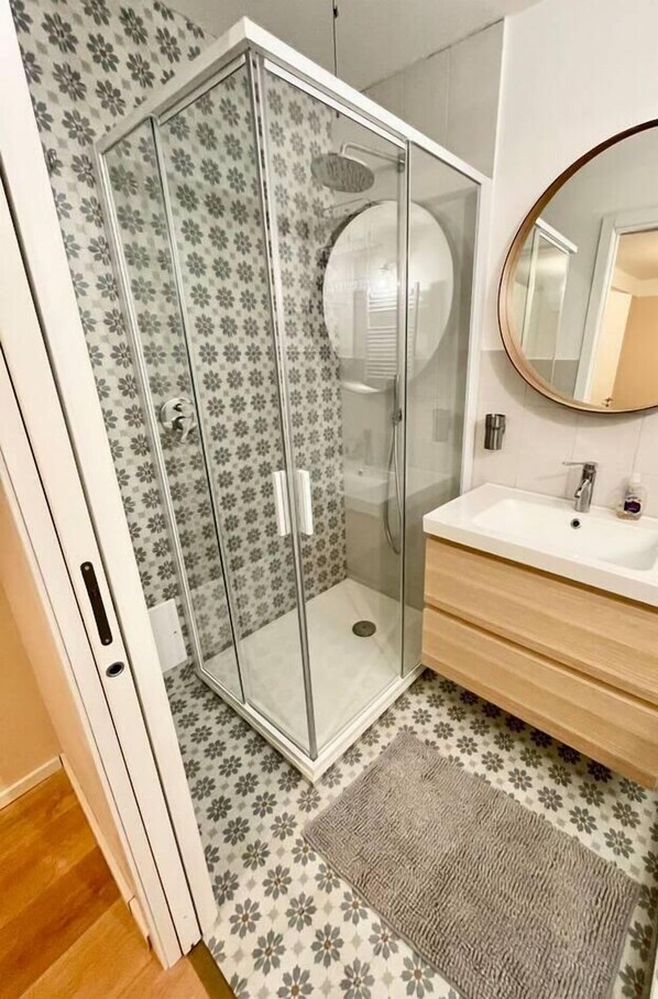 A bathroom with a glass-enclosed shower, a white sink with a wooden vanity, and patterned floor tiles.