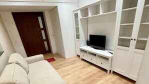 Un salon avec un canapé beige, un téléviseur posé sur un meuble blanc et un plancher en bois.