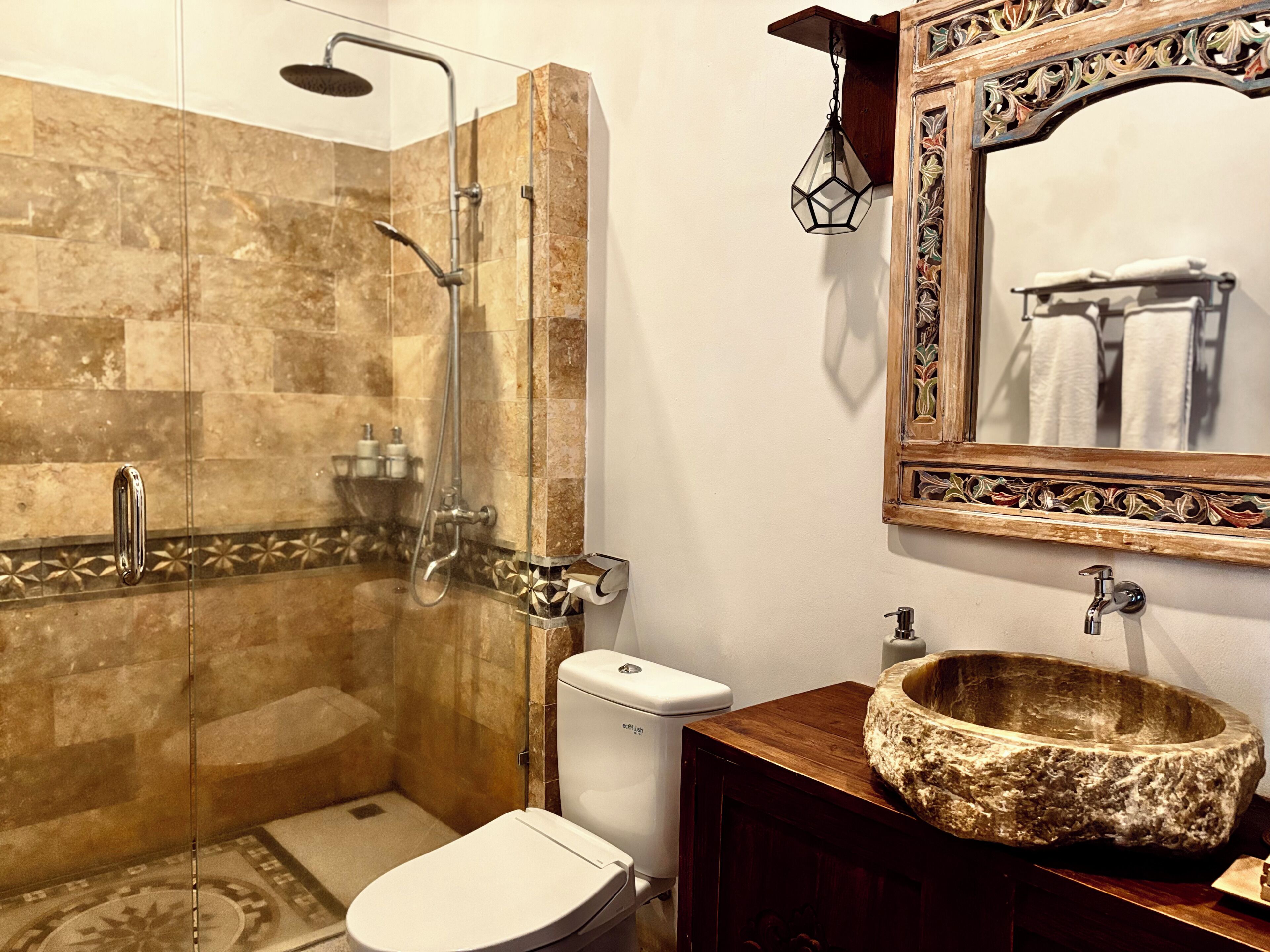 A bathroom with a glass-enclosed shower, a toilet, and a vanity with a stone basin.