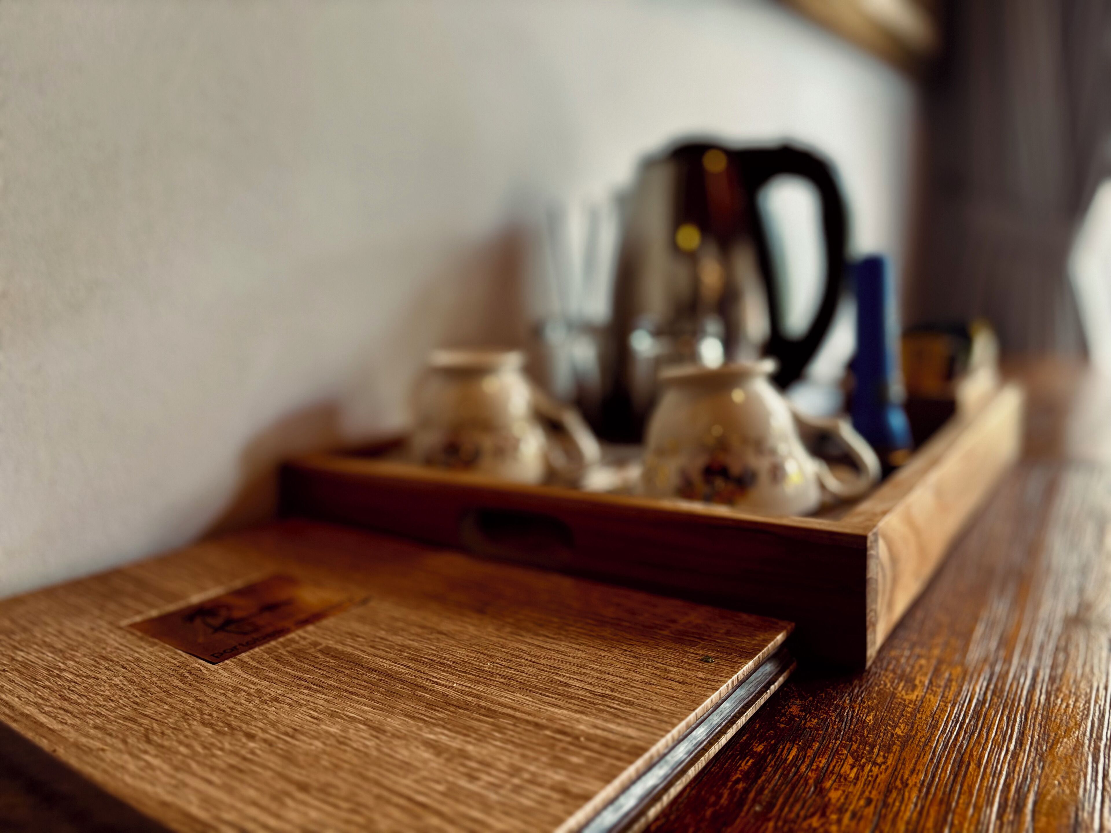 A wooden tray with a label, a kettle, and a blue object on a table.