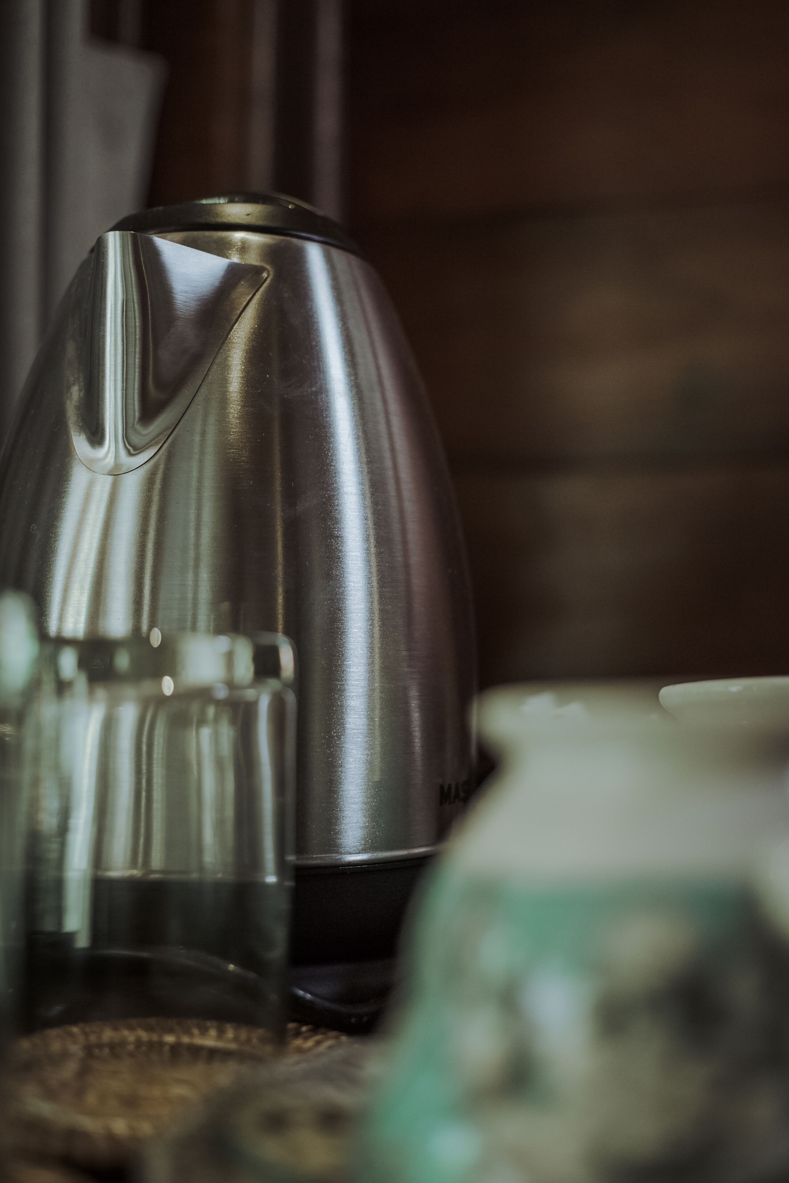 A metallic object with a reflective surface, possibly a part of a kitchen appliance, placed on a surface with a blurred background.