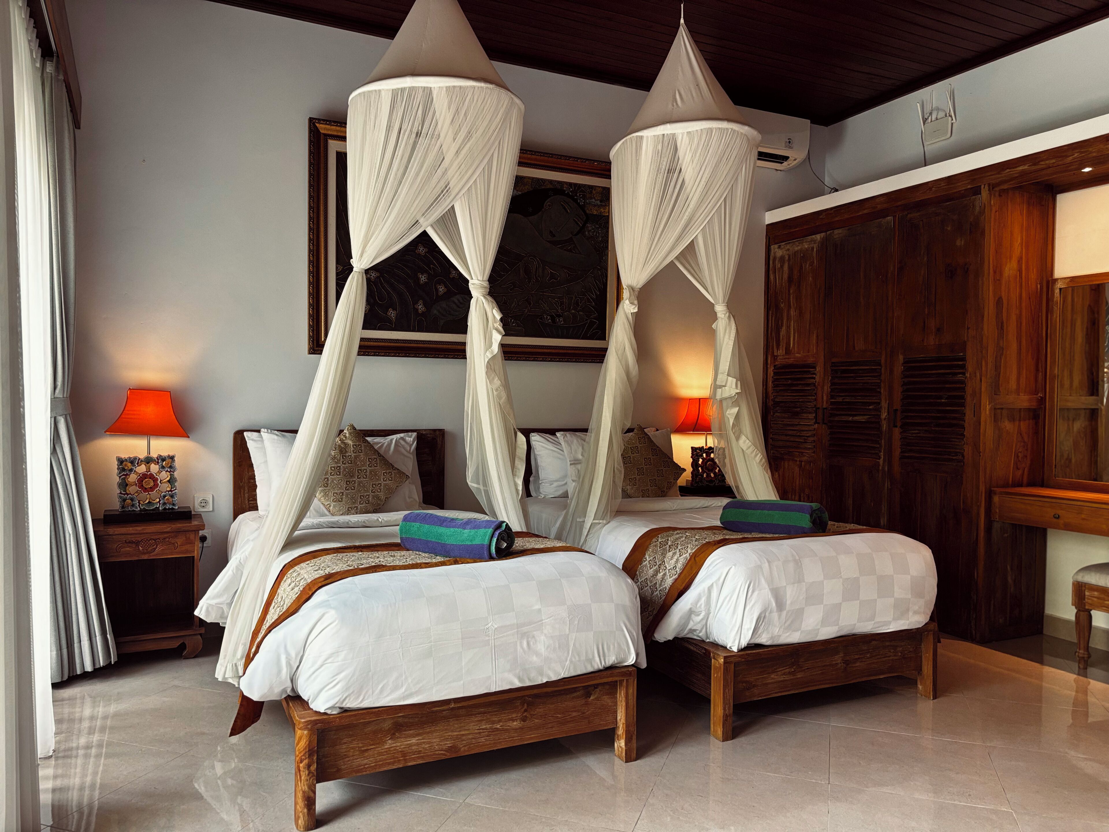 A bedroom with two beds, a nightstand, a lamp, and a wardrobe.