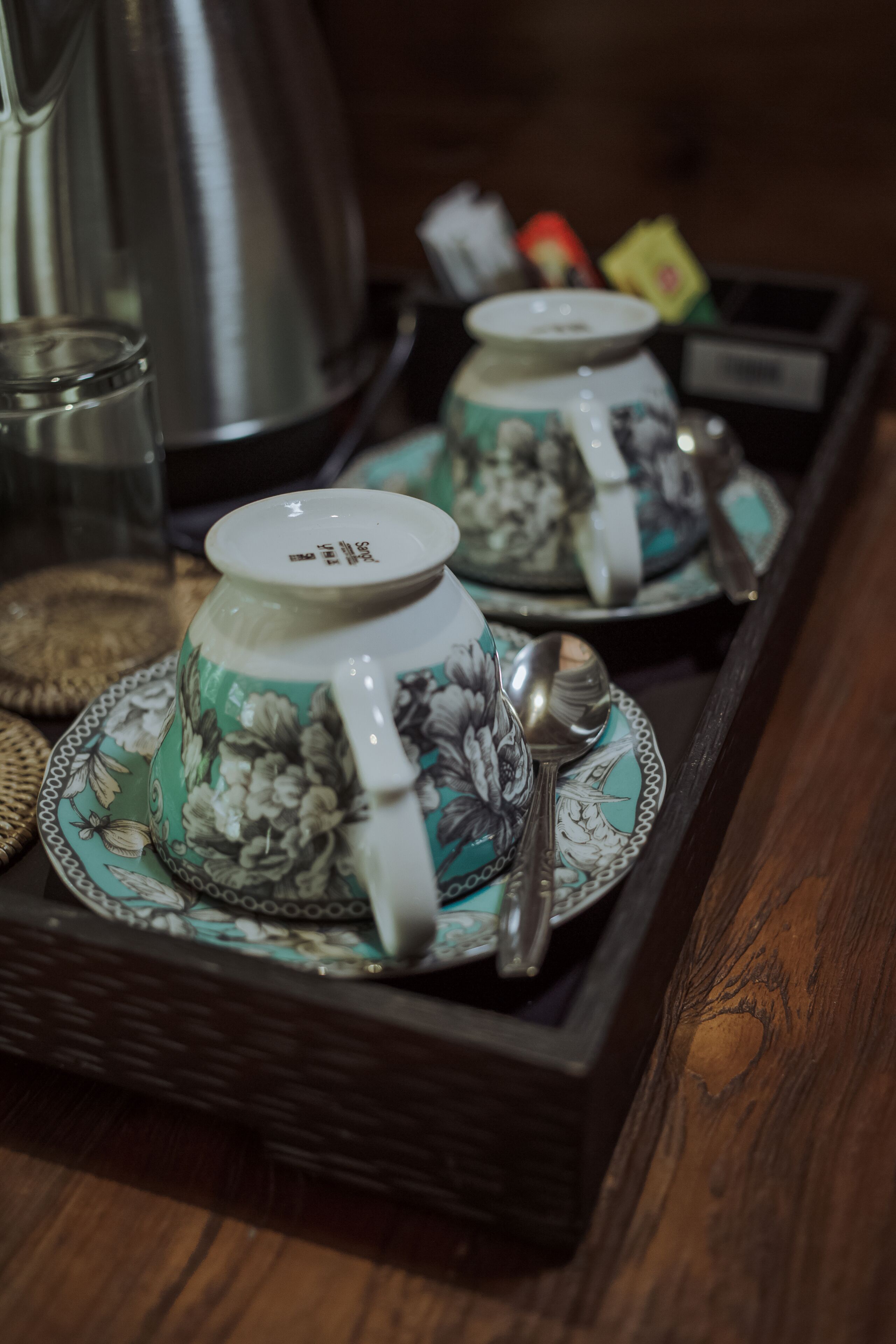 A tray with two teapots and spoons, placed on a wooden surface.