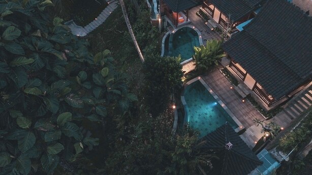 An aerial view of a resort with a swimming pool, surrounded by lush vegetation and traditional architecture.