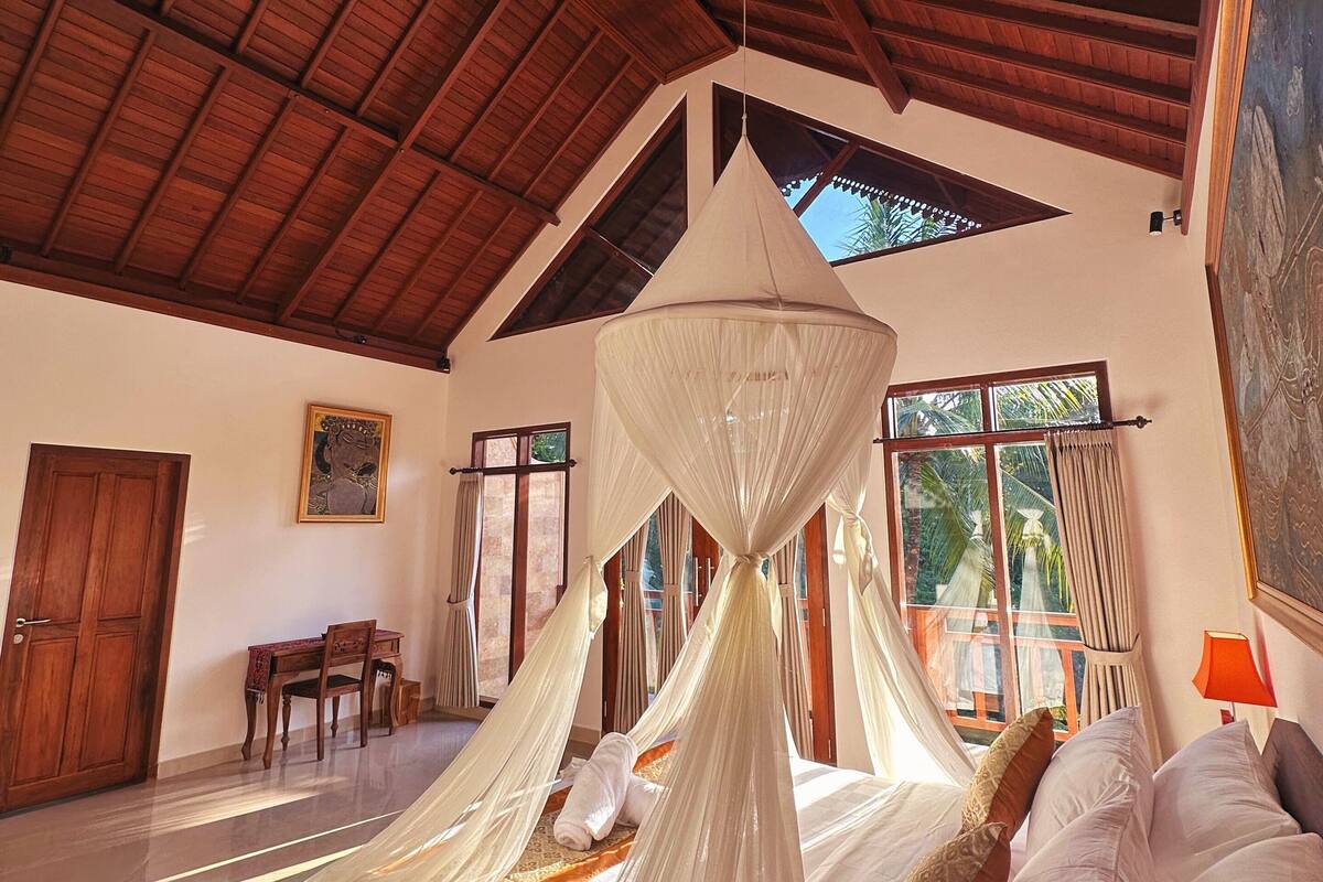 Une chambre à coucher avec un lit à baldaquin, un plafond en bois et un coin repas comprenant une table et des chaises.
