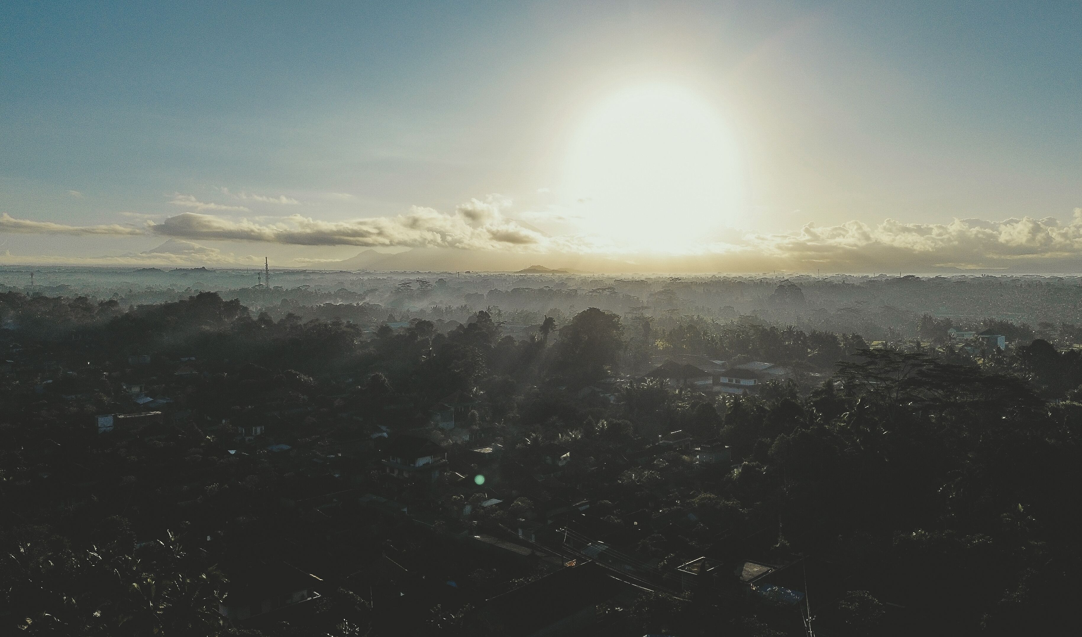 A cityscape with a prominent sun in the sky, a bridge, and a distant mountain.