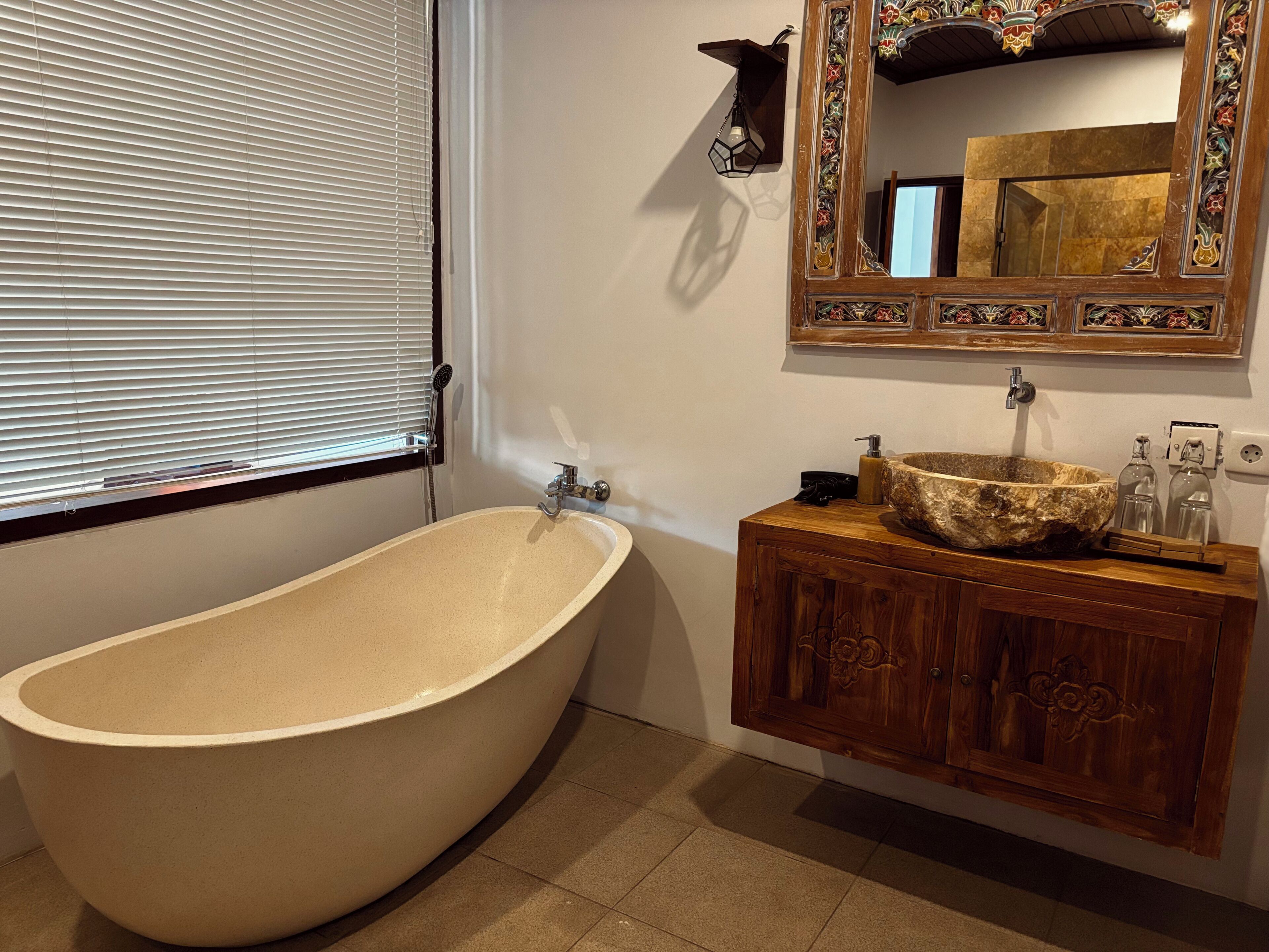 A bathroom with a freestanding bathtub, a wooden vanity with a sink, and a decorative mirror with a floral frame.