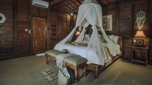 A wooden room with a bed under a canopy, a bench, a nightstand with a lamp, and an air conditioning unit.