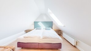 Une petite chambre mansardée, lumineuse, avec un lit simple, une fenêtre et un radiateur.