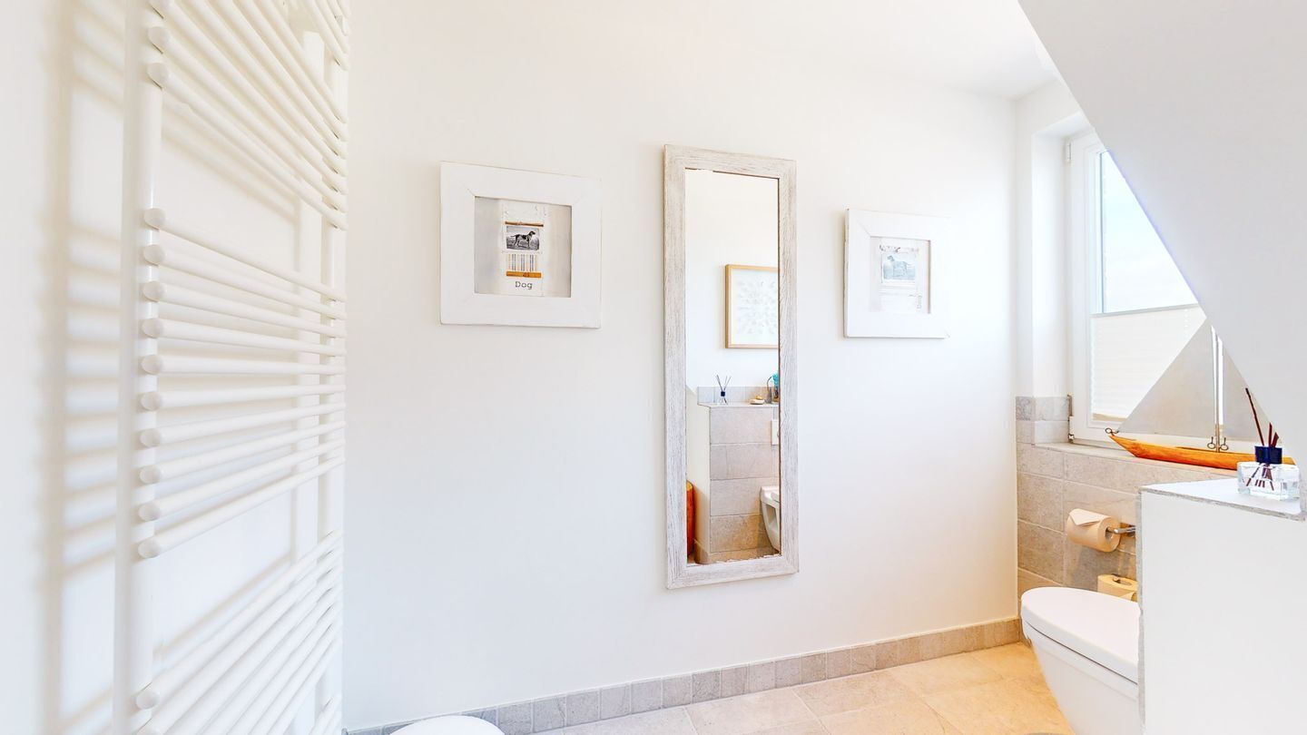 A modern bathroom with a large mirror, framed pictures, and a white radiator.