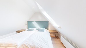 Un dormitorio moderno y minimalista con techo inclinado, cama con ropa de cama blanca y cabecera estampada en azul.