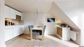 Cocina compacta con armarios blancos, una mesa de comedor de madera y un radiador en un mueble pequeño.