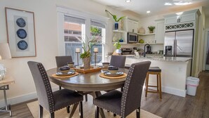 A modern kitchen with white cabinets, stainless steel appliances, and a dining area with a round table and chairs. - Brand New Craftsman 2BR 2BA Home in Denver Heights (San Antonio)