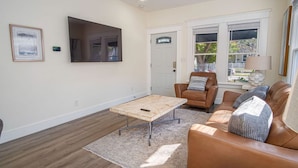 A living room with a brown leather sofa, a wooden coffee table, and a TV mounted on the wall. - Brand New Craftsman 2BR 2BA Home in Denver Heights (San Antonio)