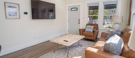 A living room with a brown leather sofa, a wooden coffee table, and a TV mounted on the wall.