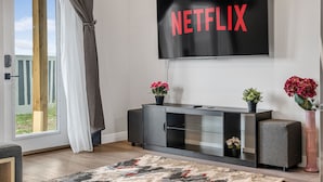 A modern living room with a large flat-screen TV mounted on the wall displaying the word "NETFLIX". - Sunny Walk-out Unit | Free HiSpeed WiFi & Parking | Near Grocery (Calgary)