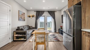 A compact living space with a dining area, a sofa, a bookshelf, and a modern kitchen with a refrigerator. - Sunny Walk-out Unit | Free HiSpeed WiFi & Parking | Near Grocery (Calgary)