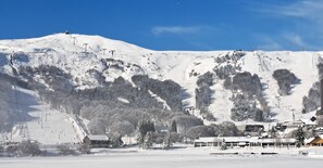 Montanha coberta de neve com teleféricos e um pequeno edifício na base.