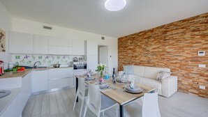 A modern kitchen with white cabinets, a wooden dining table set with plates, glasses, and a vase of flowers.