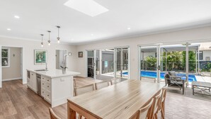 A modern kitchen with a central island, dining area with wooden furniture, and a view of a swimming pool. - 11 Esprit Drive - Rainbow Shores. Gorgeous beach house. Walk to beach (Rainbow Beach)