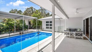 A modern outdoor pool area with a glass balustrade, a covered seating area, and a view of the surrounding greenery. - 11 Esprit Drive - Rainbow Shores. Gorgeous beach house. Walk to beach (Rainbow Beach)