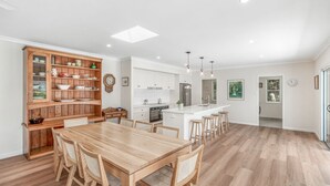 A modern kitchen with white cabinetry, a wooden dining table, and a built-in island with stools. - 11 Esprit Drive - Rainbow Shores. Gorgeous beach house. Walk to beach (Rainbow Beach)