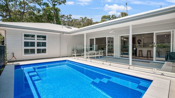 Et moderne hus med swimmingpool, store skydedøre og en patio.