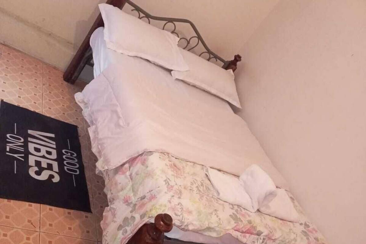 A small, single-bed room with a metal frame, a floral bedspread, and a sign on the wall.