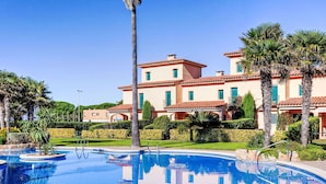 A large swimming pool with a clear blue water surface, surrounded by well-maintained greenery and palm trees.