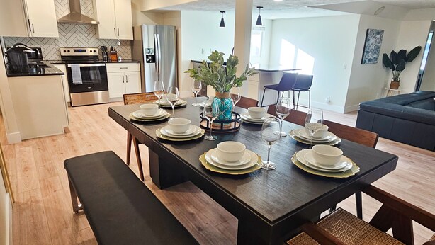 A modern kitchen with white cabinets, stainless steel appliances, and a dining area set for six with a long table, chairs, and a bench.
