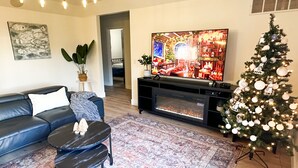 A living room with a black leather sofa, a coffee table, a fireplace, a television, and a Christmas tree.