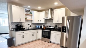 A modern kitchen with white cabinets, a stainless steel refrigerator, a microwave, a stove, and a sink.