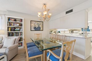 Una cocina moderna con una isla central, armarios blancos y un comedor con una mesa de vidrio y sillas de madera.