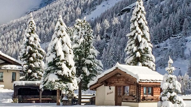 Ein schneebedecktes Blockhaus mit Holzfassade und einem Schild mit der Aufschrift 'Stadel'.