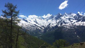 Eine gebirgige Landschaft mit schneebedeckten Gipfeln, blauem Himmel und einem markanten Felsen im Vordergrund.