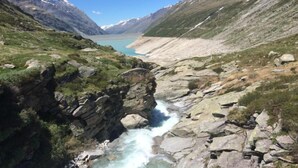 Eine Berglandschaft mit einem Fluss, der durch eine felsige Schlucht fließt, umgeben von schneebedeckten Gipfeln und blauem Himmel.