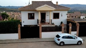 Une maison à deux étages, avec un toit en tuiles, un balcon et une voiture garée devant.