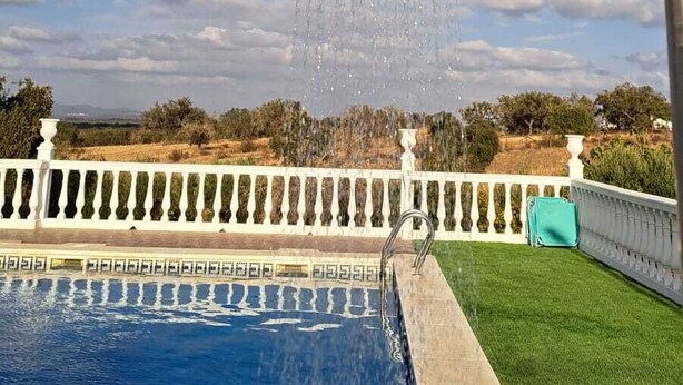 Una piscina con una fuente de agua, rodeada por una cerca blanca y follaje.