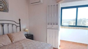 Un dormitorio con cama, aire acondicionado, ventana con cortinas y vista al exterior.