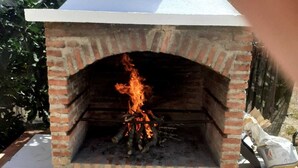 Un horno de ladrillo al aire libre con revestimiento blanco y fuego visible en su interior.