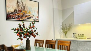 A dining area with a glass table, wooden chairs, a vase with red fruits, and a painting on the wall. - Lanha Hotel-Homestay (Hanoi)