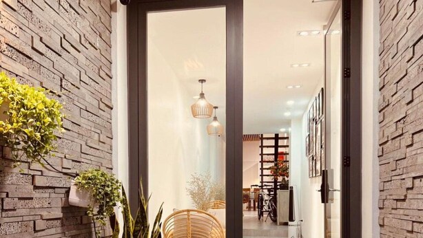 A modern entrance with a wooden ceiling, a brick wall, and a glass door leading to a well-lit interior. - Lanha Hotel-Homestay (Hanoi)