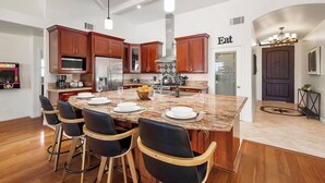 A modern kitchen with a central island, bar stools, and a dining area. - The Tulum House (San Diego)