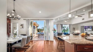 A spacious open-plan living area with a dining table, kitchen island, and large windows. - The Tulum House (San Diego)