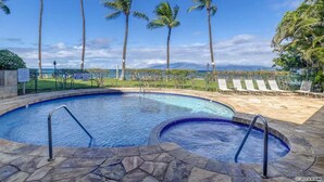 A swimming pool with two hot tubs, surrounded by palm trees and lounge chairs.