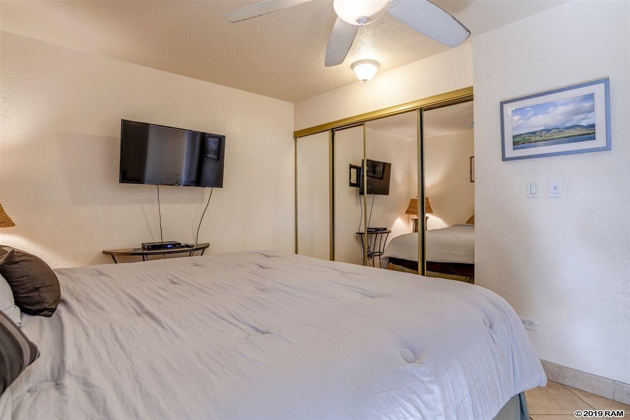 A bedroom with a bed, a ceiling fan, a flat-screen TV mounted on the wall, and a sliding door closet.