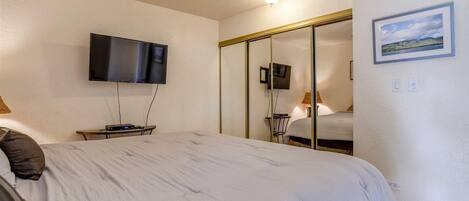 A bedroom with a bed, a ceiling fan, a flat-screen TV mounted on the wall, and a sliding door closet.