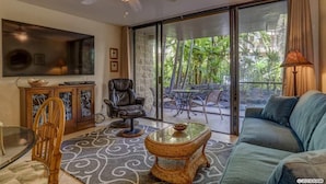 A spacious living area with a ceiling fan, a large TV, a sofa, a dining table, and a glass coffee table.