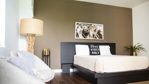 A modern bedroom with a bed, a sofa, a lamp, a picture on the wall, and a small plant.