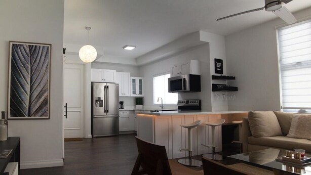 A modern kitchen with white cabinets, a stainless steel refrigerator, and a bar area with stools.